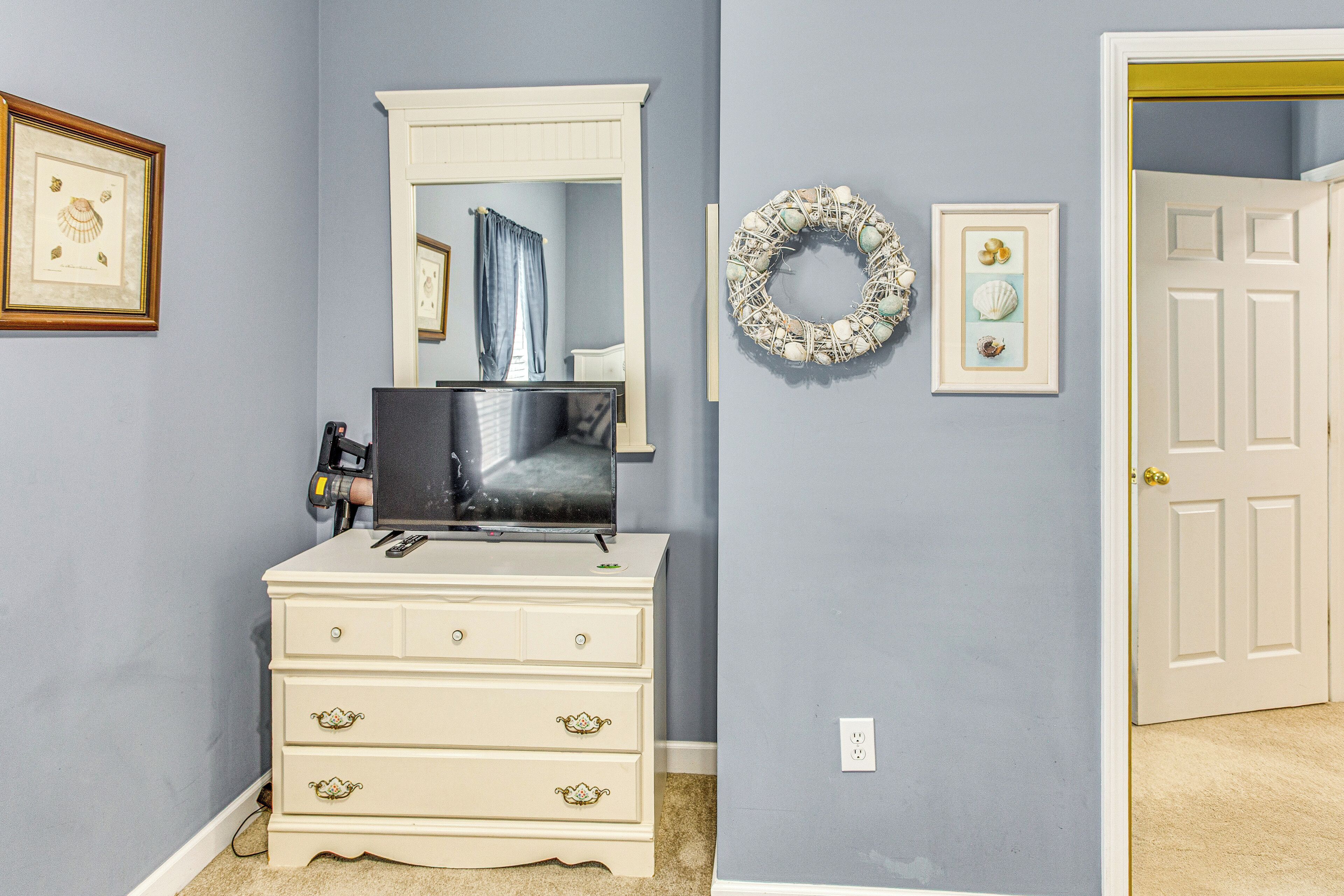 A room with a white dresser, a mirror, a television, and a door.
