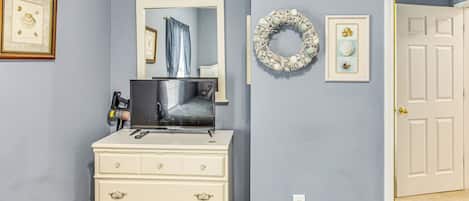 A room with a white dresser, a mirror, a television, and a door.