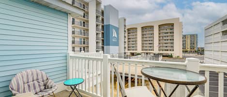 A balcony with a striped chair, a small round table, and a view of a hotel building with balconies and a sailboat logo.