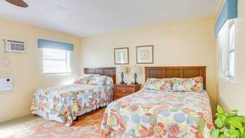 A bedroom with two beds, a nightstand, a wall-mounted air conditioner, and a window with blinds.