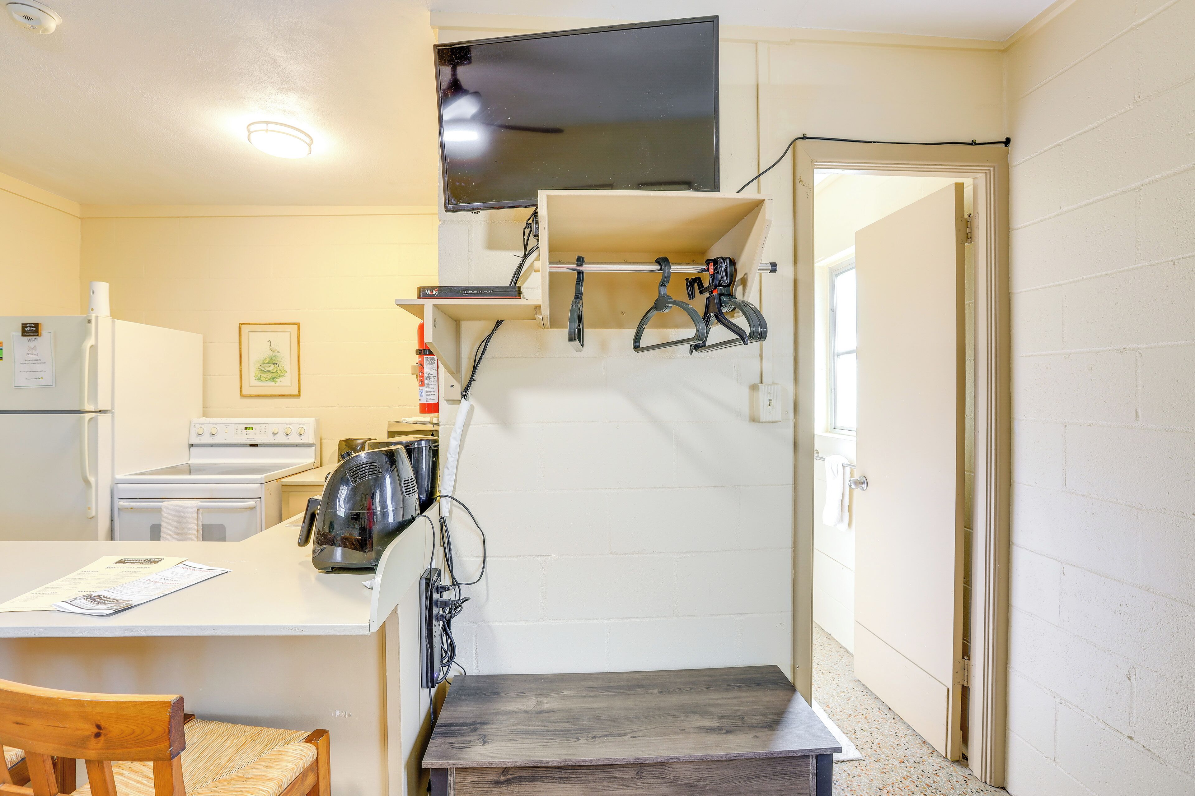 A compact kitchen with a refrigerator, stove, and microwave. There is a wooden chair and a small table.