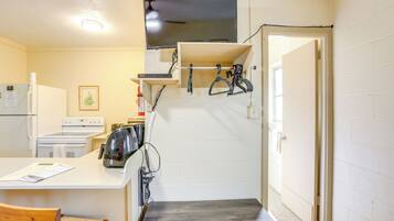 A compact kitchen with a refrigerator, stove, and microwave. There is a wooden chair and a small table.