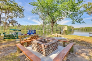 Un camping con un brasero de ladrillo, mesas de picnic y vista al lago.