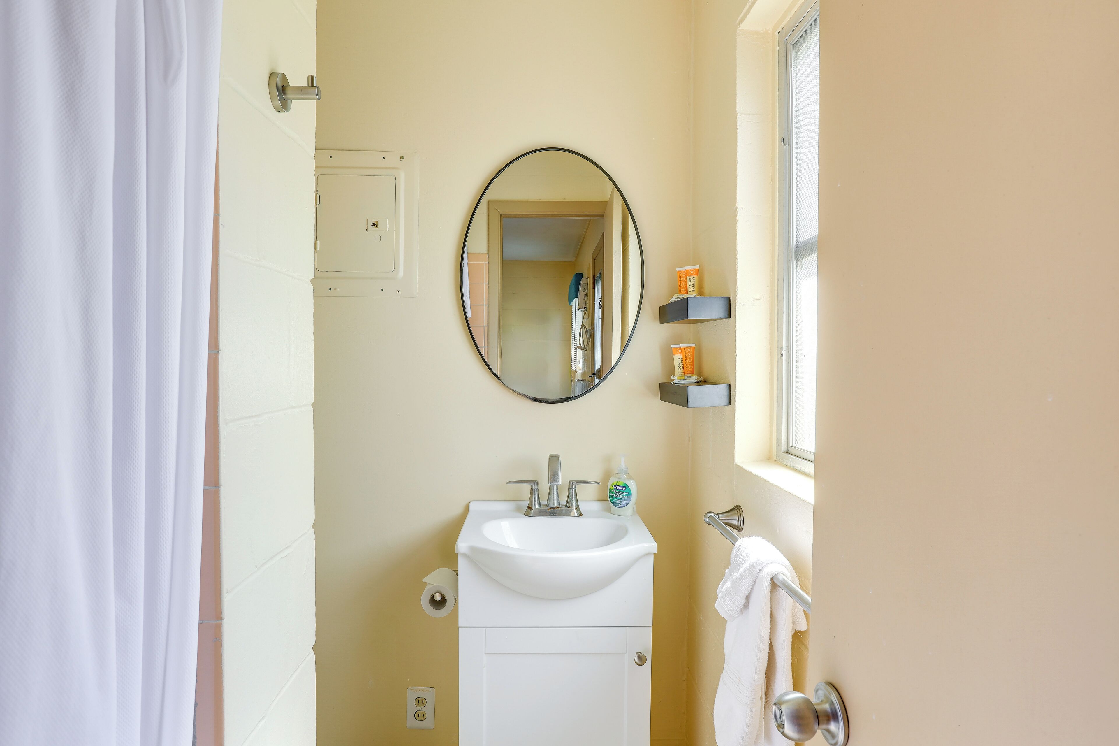 A bathroom with a white sink, a mirror, a towel rack, and a window.
