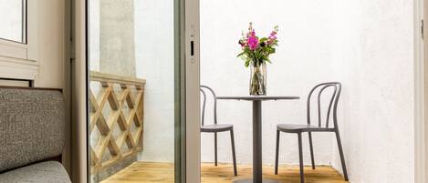 A room with a wooden floor, a round table with chairs, a vase with flowers, and a cushioned bench.