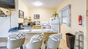 A compact kitchen with a dining area, a TV mounted above the counter, and a fire extinguisher on the wall. - Lanai & Fire Pit: Riverfront Studio in Chiefland! (Chiefland)
