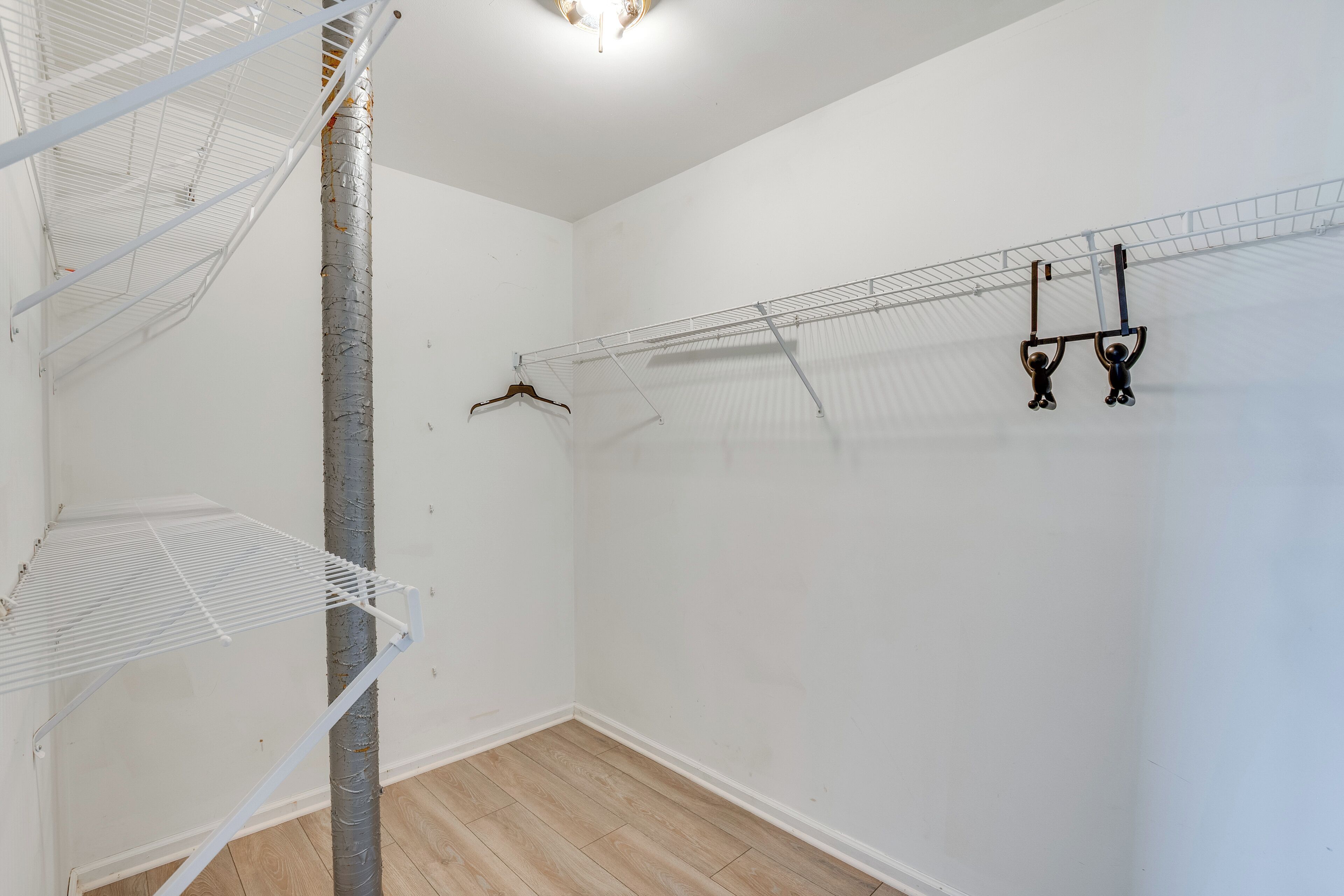 A room with white walls, a wooden floor, and a metal rack with clothes hanging.