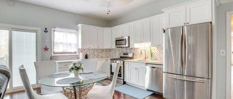 A modern kitchen with white cabinets, stainless steel appliances, a glass dining table, and a ceiling fan.