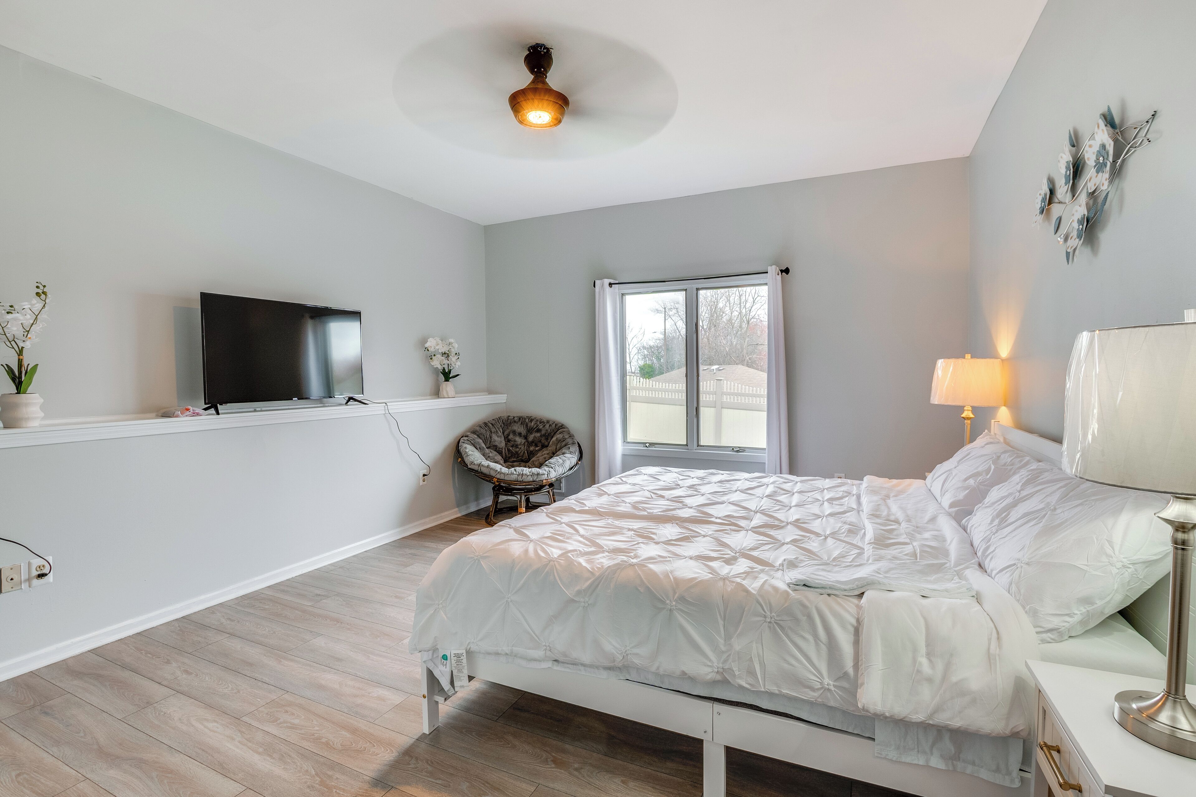 Un dormitorio con cama, televisión, silla, ventana y lámpara.