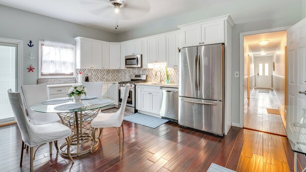A modern kitchen with white cabinets, stainless steel appliances, and a dining area with a glass table and white chairs. - 5 Mi to Rutgers University: New Jersey Guest Suite (South River)