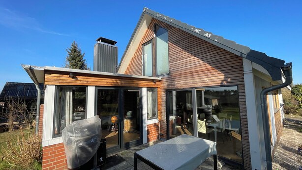 Une maison moderne dotée d’une grande porte vitrée, d’un revêtement en bois et d’un toit équipé de panneaux solaires.