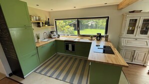 Une cuisine moderne avec des meubles de couleur verte, un plan de travail en bois, un four encastré et une fenêtre donnant sur un jardin.
