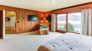 Un'ampia camera da letto con un letto grande, una sedia in legno con un cuscino, una televisione a parete e un balcone con vista sull'acqua.