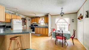 A kitchen with wooden cabinets, a refrigerator, a dining table with chairs, and a window with curtains. - Creekside Retreat in the Adirondacks: Swim & Hike! (Forestport)