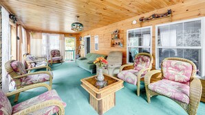 A cozy wooden cabin interior with wicker furniture, a glass coffee table, and a view through large windows. - Creekside Retreat in the Adirondacks: Swim & Hike! (Forestport)