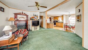 A spacious living room with a fireplace, a television, and a dining area with a kitchen in the background. - Creekside Retreat in the Adirondacks: Swim & Hike! (Forestport)