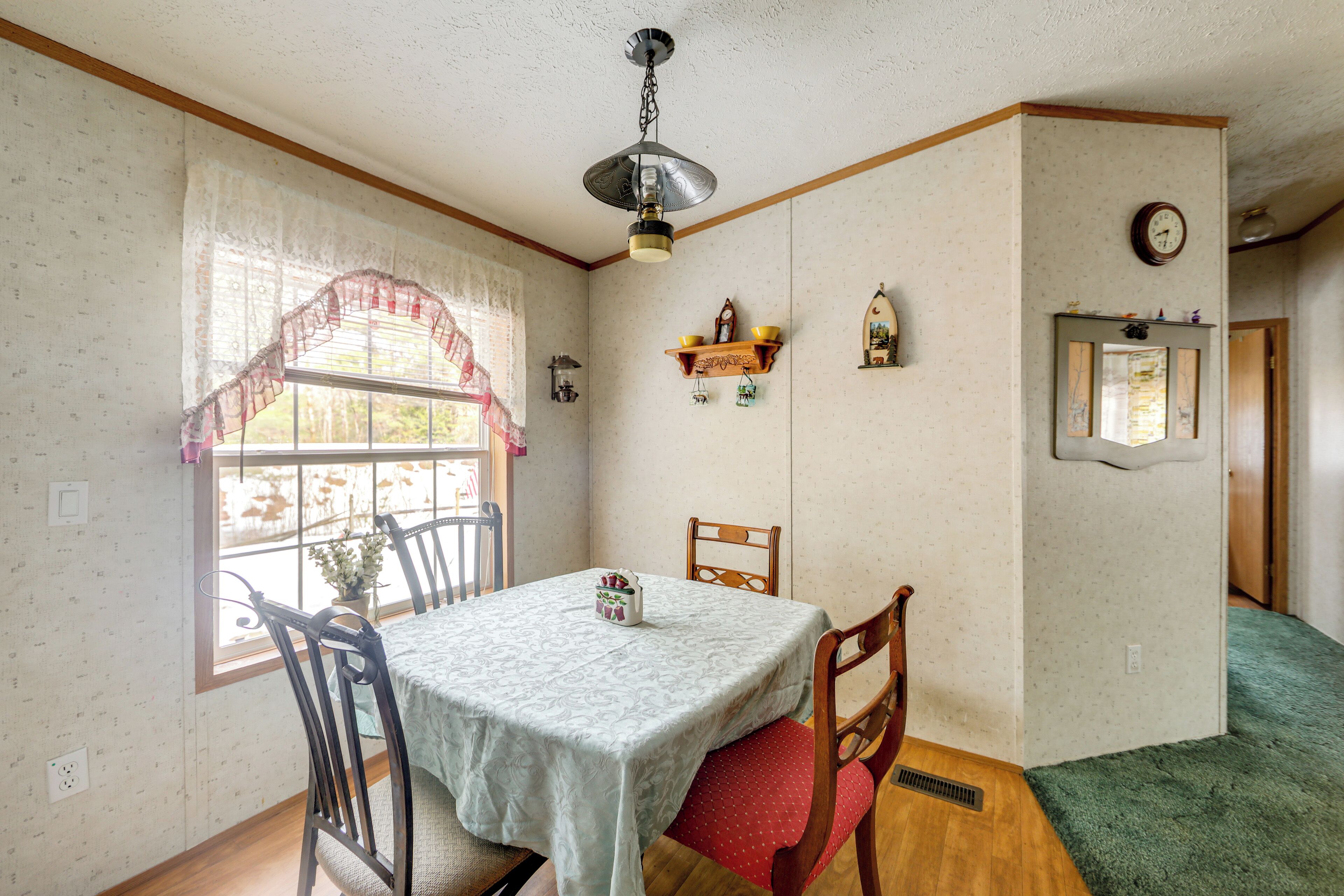 A dining room with a table set for four, wooden chairs, a window with lace curtains, and a ceiling fan.