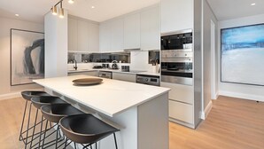 A modern kitchen with white cabinetry, a central island with stools, stainless steel appliances, and pendant lighting.