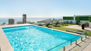 A rooftop pool with a city view, lounge chairs, and a green wall.