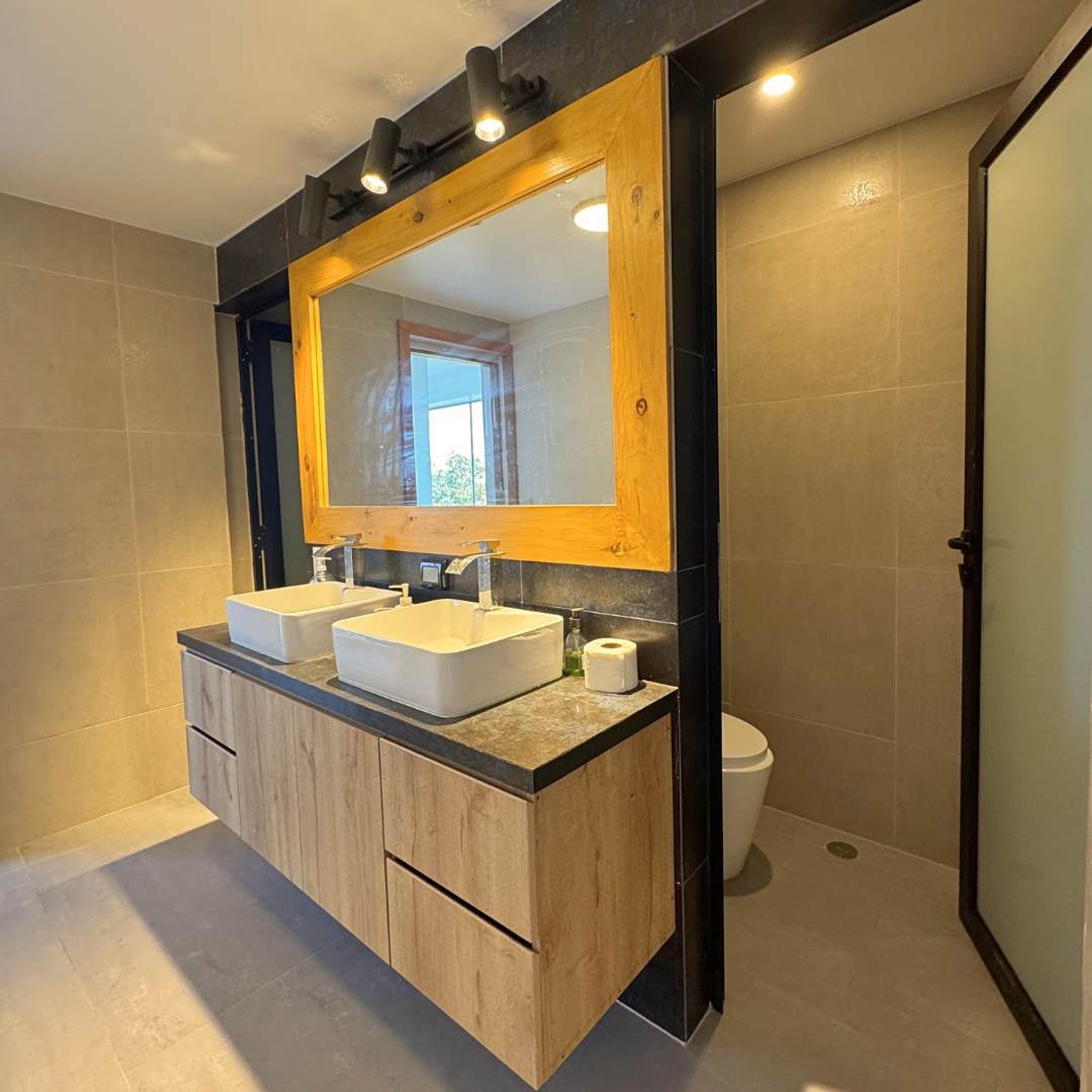 A modern bathroom with two sinks, a large mirror, and a toilet.
