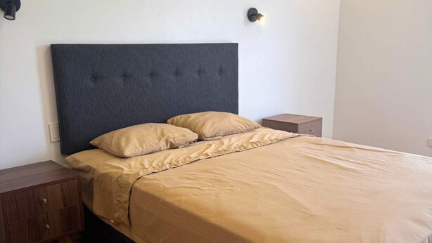 A neatly made bed with a dark headboard, a wooden nightstand, and a small bedside table. - Hop Honolulu Exclusiva Oasis y Playa en Chincha (El Carmen)