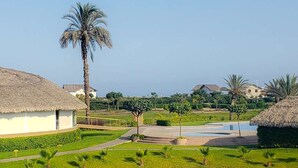 Ein Resort mit strohgedeckten Gebäuden, einem zentral gelegenen Pool und gepflegten Rasenflächen.
