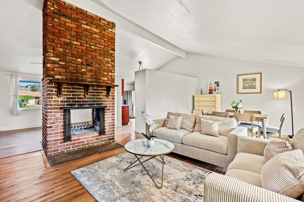 A living room with a brick fireplace, a sofa set, a dining area, and a framed picture on the wall. - Cozy Family Retreat With Fireplace Spacious Yard (Duarte)
