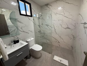 A modern bathroom with a glass-enclosed shower, a marble-tiled wall, a white sink, and a toilet. - 3BR Villa by Vistacana Rentals (Punta Cana)