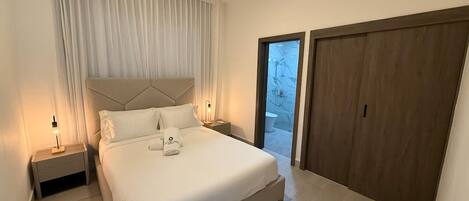 A modern bedroom with a large bed, a nightstand, a bedside lamp, and a view of the outside through a glass door.