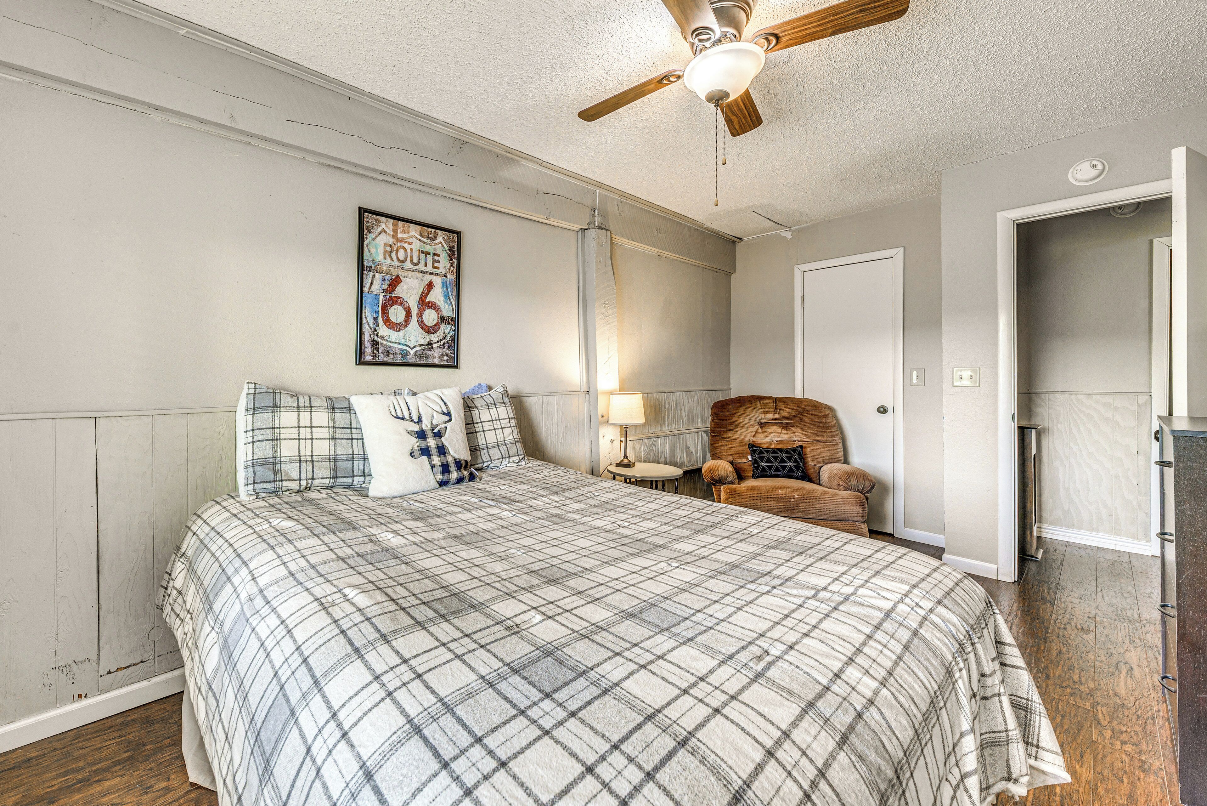 A bedroom with a large bed, a ceiling fan, a chair, and a door.