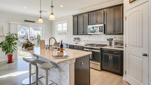 A modern kitchen with dark cabinets, a central island with bar stools, a built-in oven, and a microwave. - 3 Mi to Umstead State Park: Durham Home (Durham)