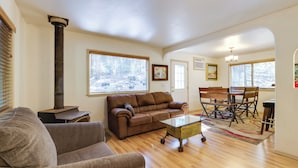 A living room with a brown leather sofa, a glass coffee table, a dining table with chairs, and a fireplace. - Walk to Dining! Peaceful Arnold Cabin w/ Deck (Arnold)