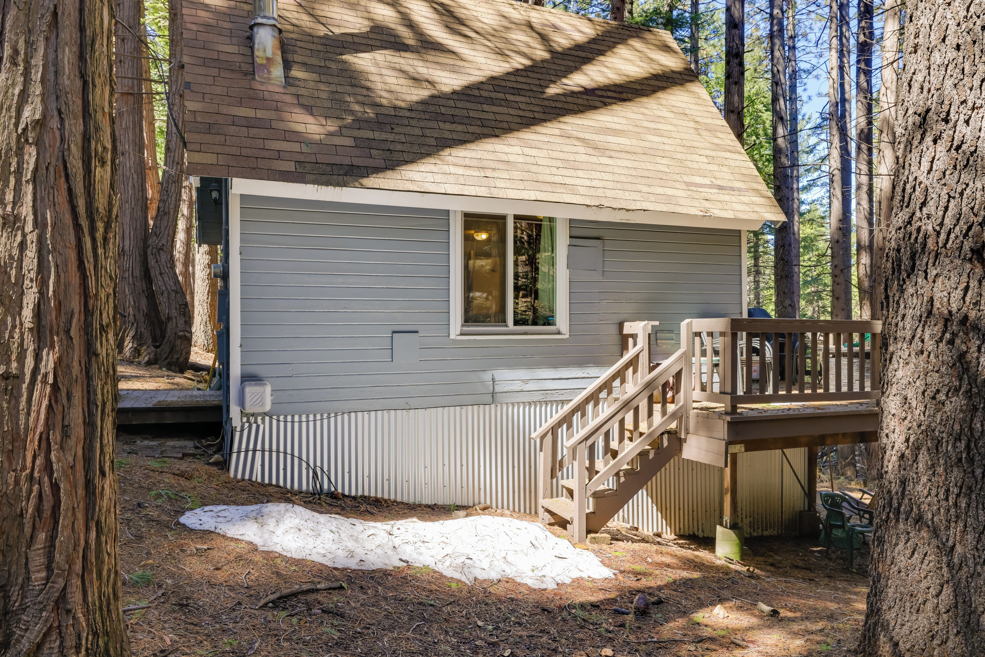 A small cabin with a wooden deck and a window, surrounded by tall trees.