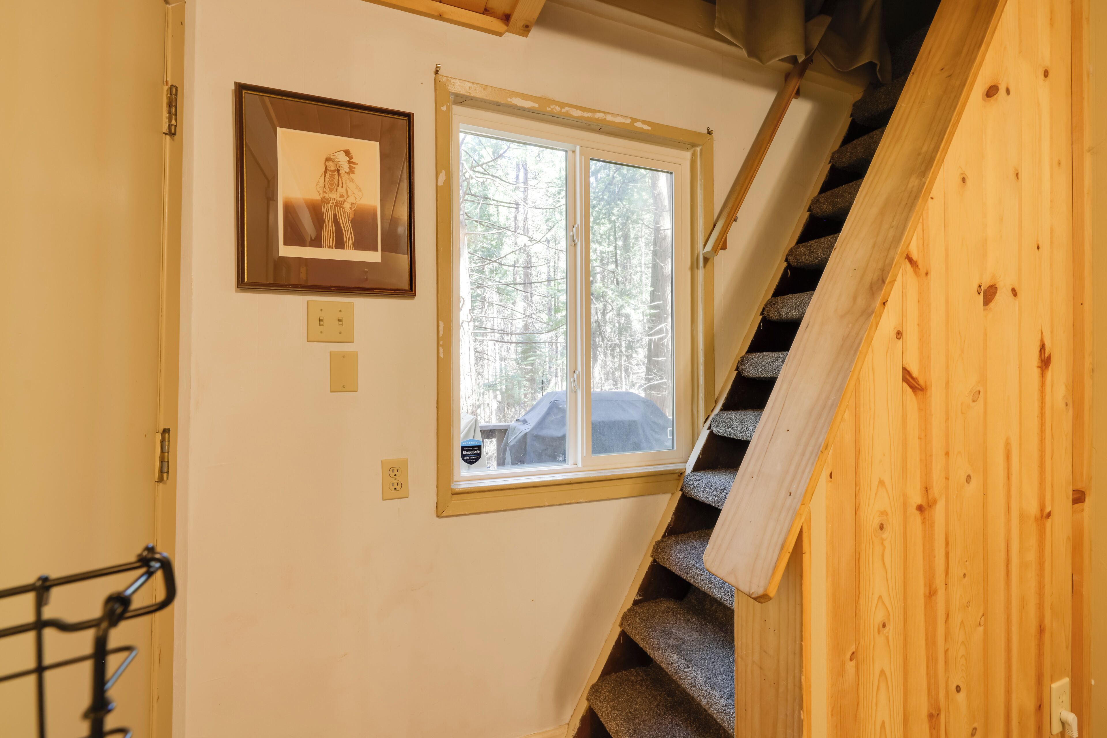 Un escalier avec des rampes en bois mène à une pièce dotée d’une fenêtre donnant sur une forêt.