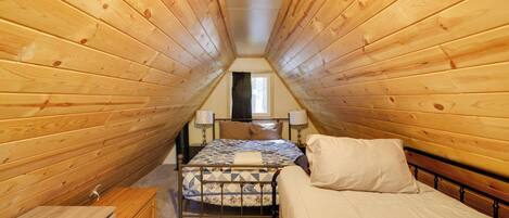 A bedroom with wooden walls, a bed with a quilt, a nightstand, and a window with curtains.