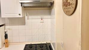 Une cuisine avec des meubles blancs, une cuisinière à gaz et un panneau mural sur lequel on peut lire : « Ma journée commence avec un café et se termine avec un verre de vin. »