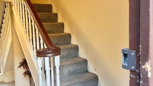 Un escalier avec une main courante en bois et des balustres blanches, menant à un palier doté d’une porte.