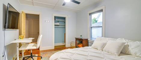 A bedroom with a bed, a desk, a chair, a ceiling fan, and a window.