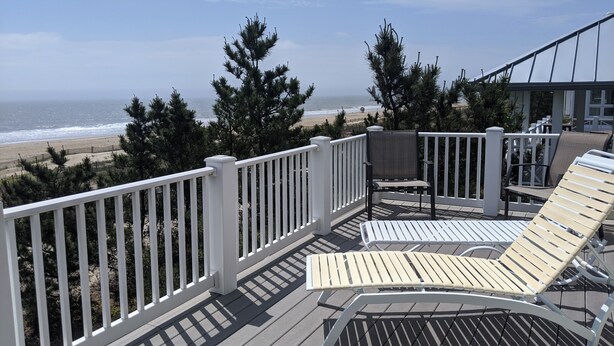 A deck with white railings, a lounge chair, and a table. - 5 Bedroom Oceanfront on a private beach (Bethany Beach)