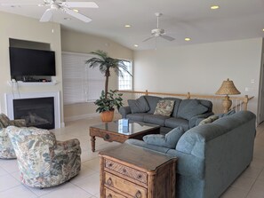 Uma sala de estar com sofá, poltronas, mesa de centro, televisão, lareira e ventilador de teto.