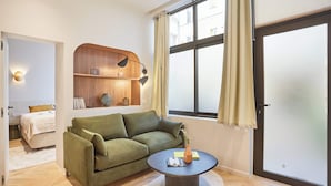 A modern living room with a green sofa, a round coffee table, and a wooden shelving unit with books and decorative items. - Superb AC Apartment Center of Paris (Paris)