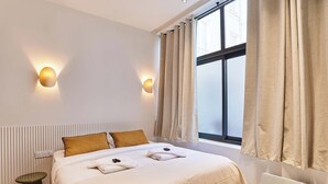 A modern hotel room with a large bed, two wall-mounted lights, a window with curtains, and a bedside table. - Superb AC Apartment Center of Paris (Paris)