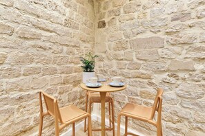 A stone-walled room with a round table and two wicker chairs.