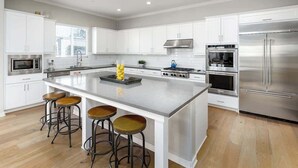 A modern kitchen with white cabinets, stainless steel appliances, a central island with stools, and a large refrigerator.