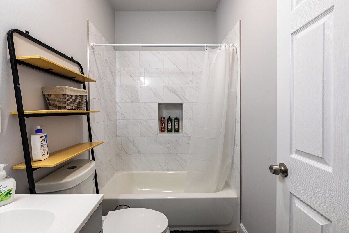 A bathroom with a shower, toilet, and a shelf with toiletries.
