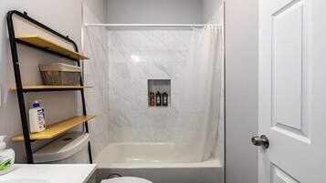 A bathroom with a shower, toilet, and a shelf with toiletries.
