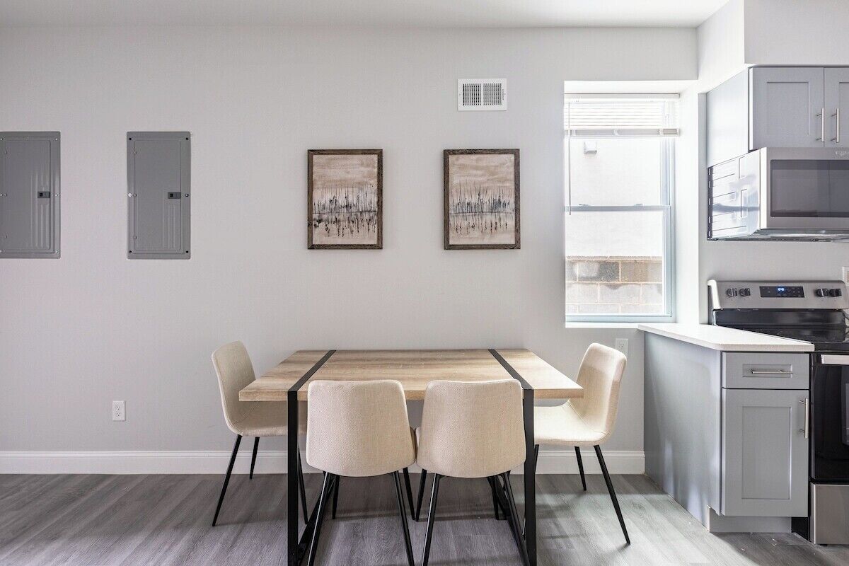 A modern kitchen with a built-in oven and microwave, a dining area with a wooden table and four chairs, and two framed artworks on the wall.
