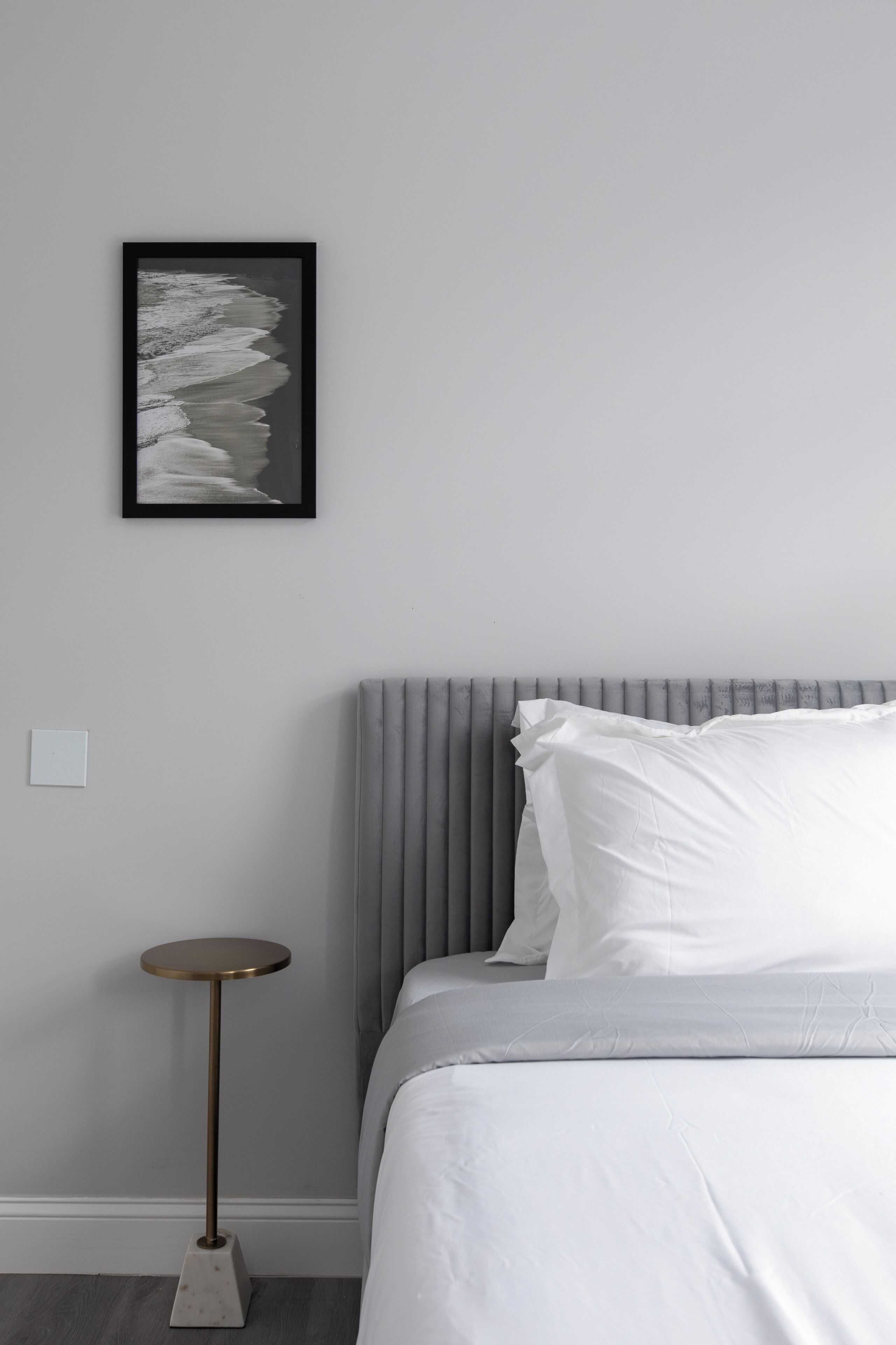 A bedroom with a bed, a bedside table, a framed picture on the wall, and a radiator.