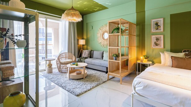 Ein modernes Wohnzimmer mit einer Couch, einem Glastisch, einem Korbstuhl, einem Holzregal und einer Pendelleuchte.