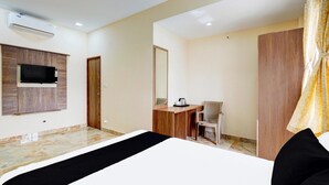 Habitación de hotel con cama, escritorio, silla, televisor montado en la pared y unidad de aire acondicionado.